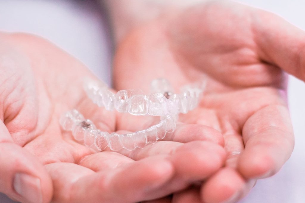 Clear aligners held in hands, representing Invisalign treatment options for orthodontics in Madison, MS at Sandifer Orthodontics.